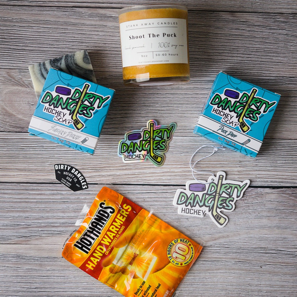 2 dirty dangles hockey soap bars, a soy wax candle, a car air freshener and hand warmers on a wood background with stickers.