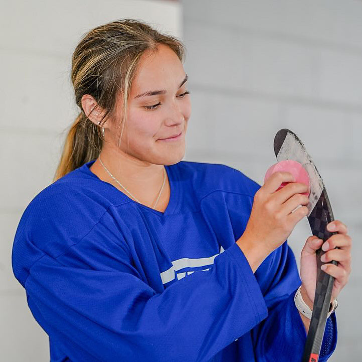 A female hockey player applying dirty dangles stick wax to her stick