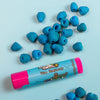 A pink stick of blue raspberry lip balm on a blue background with blue raspberries. Dirty dangles blue raspberry natural lip balm