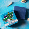 A Blue bar of dirty dangles hockey soap The Michigan scent on a blue background with a blue box with sand and shells