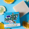 A yellow bar of dirty dangles hockey soap 2 games on the beach scent on a blue background with a blue box, lemons and lavender