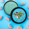 An open tin of dirty dangles sour watermelon scent stick wax on a blue background with sour watermelon candies.