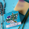 A bar  of dirty dangles hockey soap lavender lemongrass scent on a blue background with lavender.