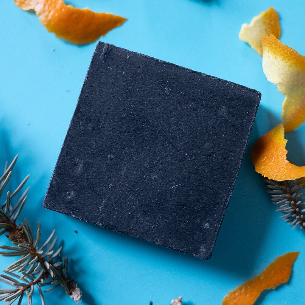 A bar of dirty dangles hockey soap puck drop scent on a blue background with pine and orange peel.