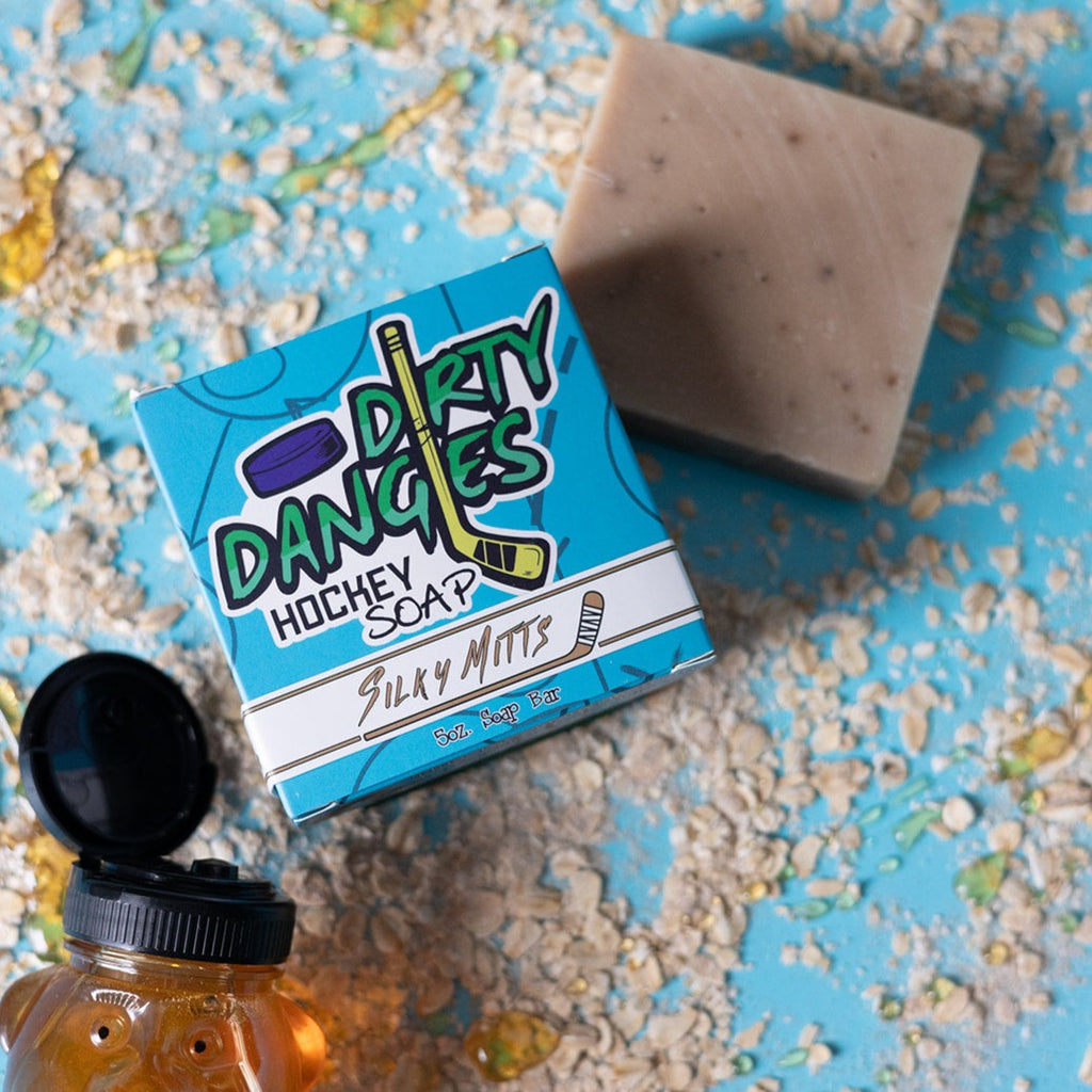A bar of dirty dangles hockey soap silky mitts scent on a blue background with honey and oats