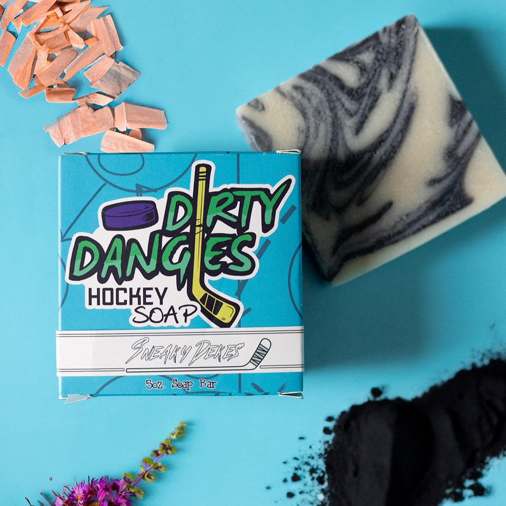 A bar of dirty dangles hockey soap silky mitts scent on a blue background with wood, charcoal and lavender