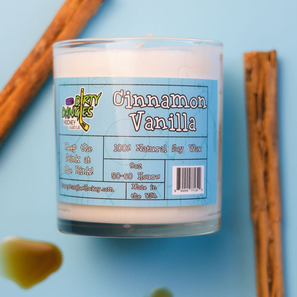 A white dirty dangles hockey cinnamon vanilla scented candle on a blue background with cinnamon sticks and vanilla.