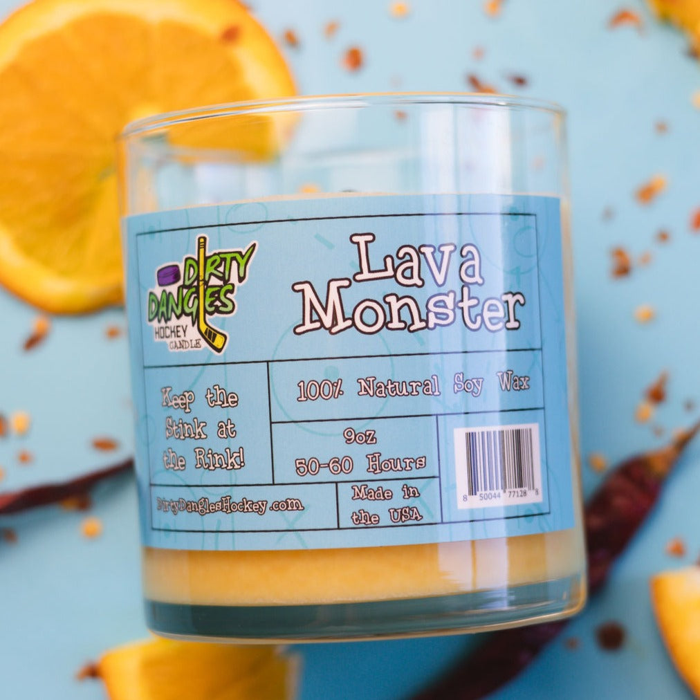 An orange dirty dangles hockey candle with a blue label on a blue background with orange slices and chili peppers. Lava monster scent