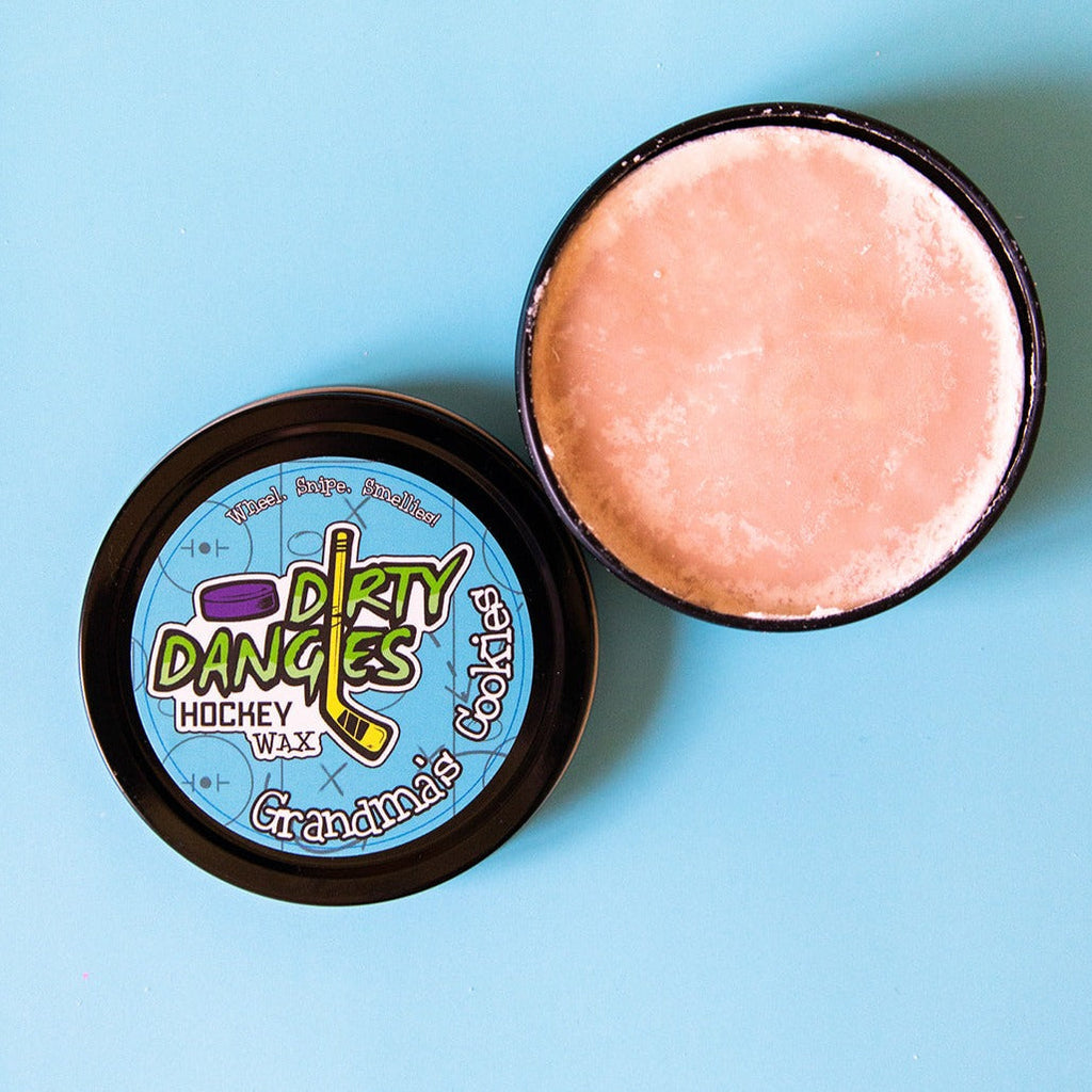 A tin of Dirty Dangles Hockey Stick Wax Grandma's Cookies scent sits open on a blue background.