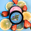 A tin of Dirty Dangles Hockey Stick Wax Strawberry Lemonade Scent sits open on a blue background surrounded by Strawberries and lemons