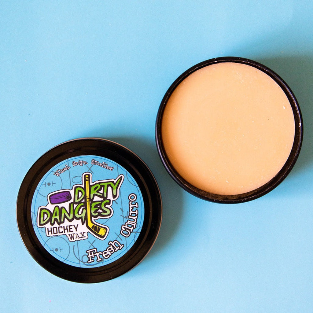 A tin of Dirty Dangles Hockey Stick Wax Fresh Churro scent sits open on a blue background.