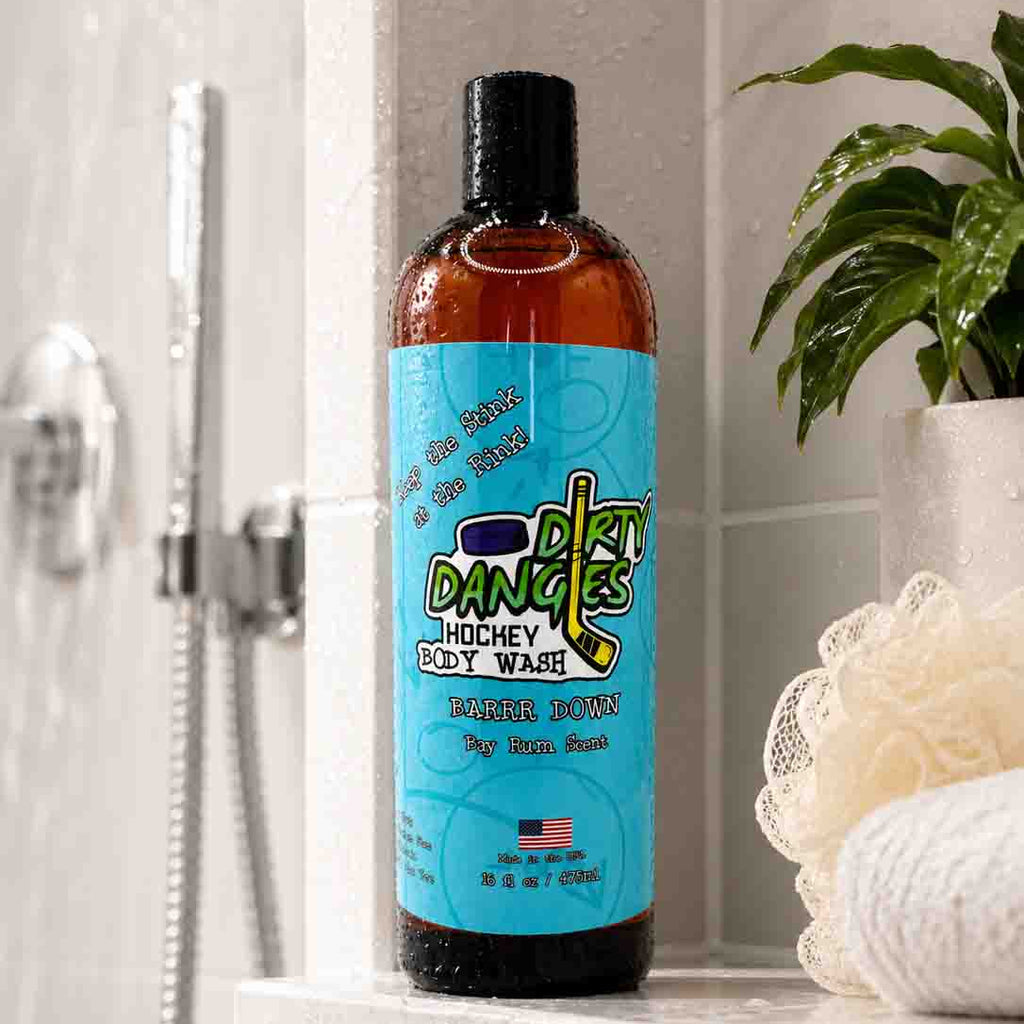 Bottle of Dirty Dancing body wash on a bathroom shelf with a plant and shower head in the background.