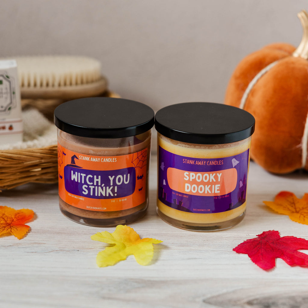 Two Halloween-themed candles  Witch You Stink and Spooky Dookie labels on a wooden surface.