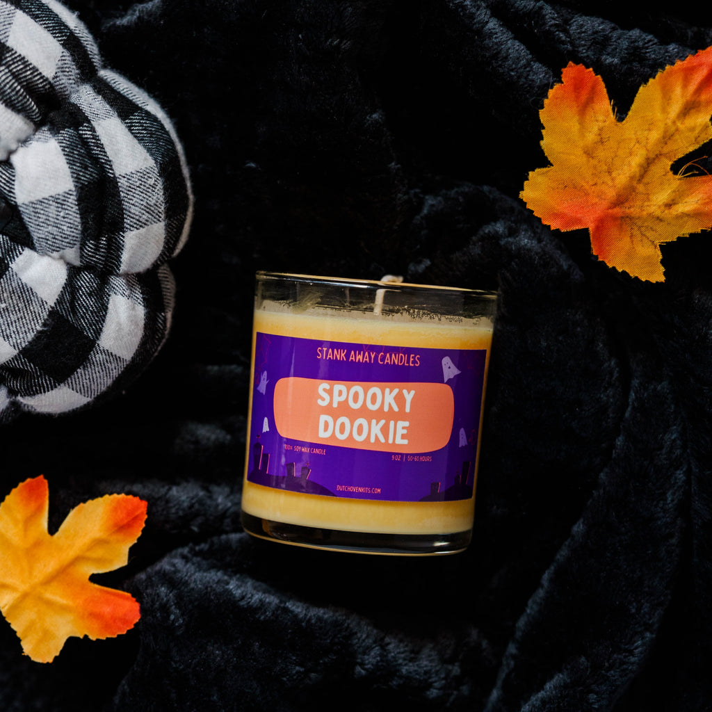 Candle labeled 'Spooky Dookie' with autumn leaves on a dark background