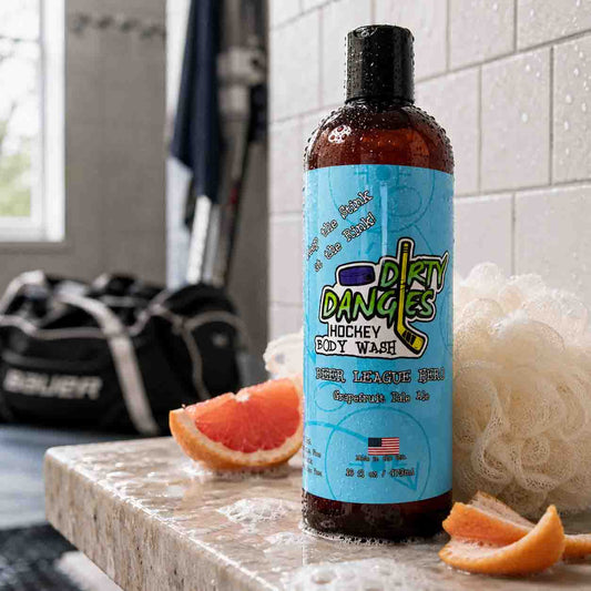 Bottle of Dirty Dangles Hockey Body Wash on a bathroom counter with grapefruit and a shower in the background.