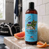 Bottle of Dirty Dangles Hockey Body Wash on a bathroom counter with grapefruit and a shower in the background.