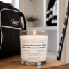 A white scented hockey candle on a wooden bench with hockey gear. Because nobody in this house wants to shower...