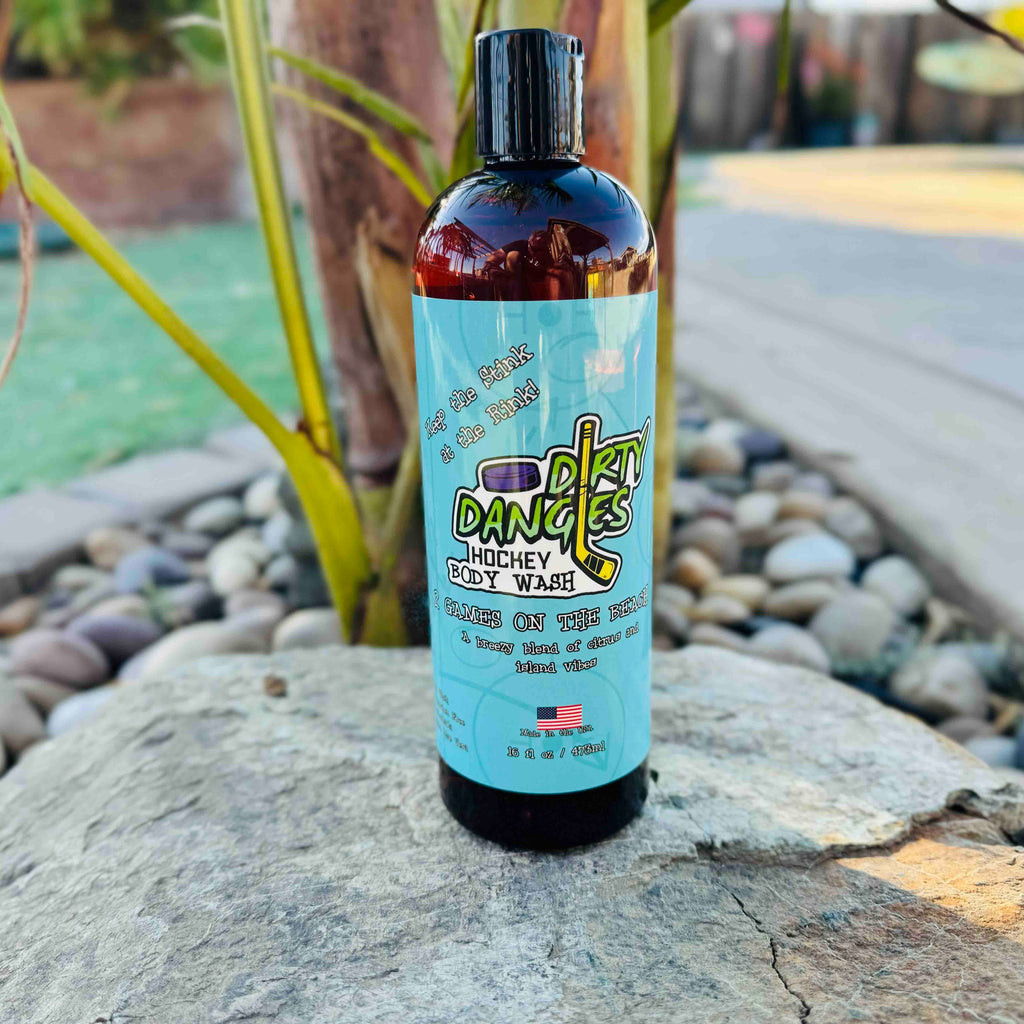A bottle of dirty dangles hockey body wash 2 games on the beach scent on a rock with a tropical background.