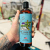 Hand holding a bottle of 'Dirty Dangles' body wash with a blurred hockey net in the background
