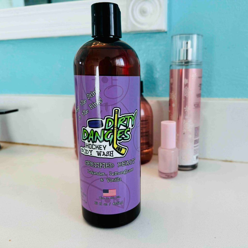 A purple bottle of dirty dangles hockey body wash certified beaut scent on a bathroom counter with cosmetics.
