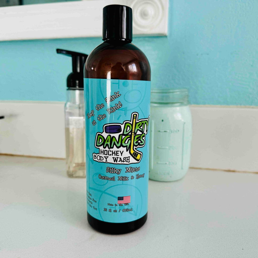 Bottle of Dirty Dangles Body Wash Silky Mitts scent on a bathroom counter with a blue background.