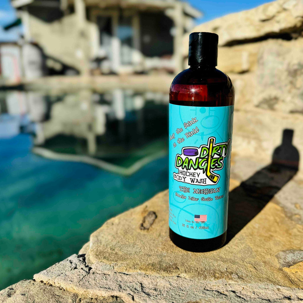 A bottle of dirty dangles body wash  The Michigan scent sitting on some rocks with water in the background