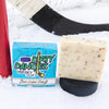 A cream and orange soap bar sits on a snowy hockey background. Dirty dangles hockey soap. Beer League Hero Scent.