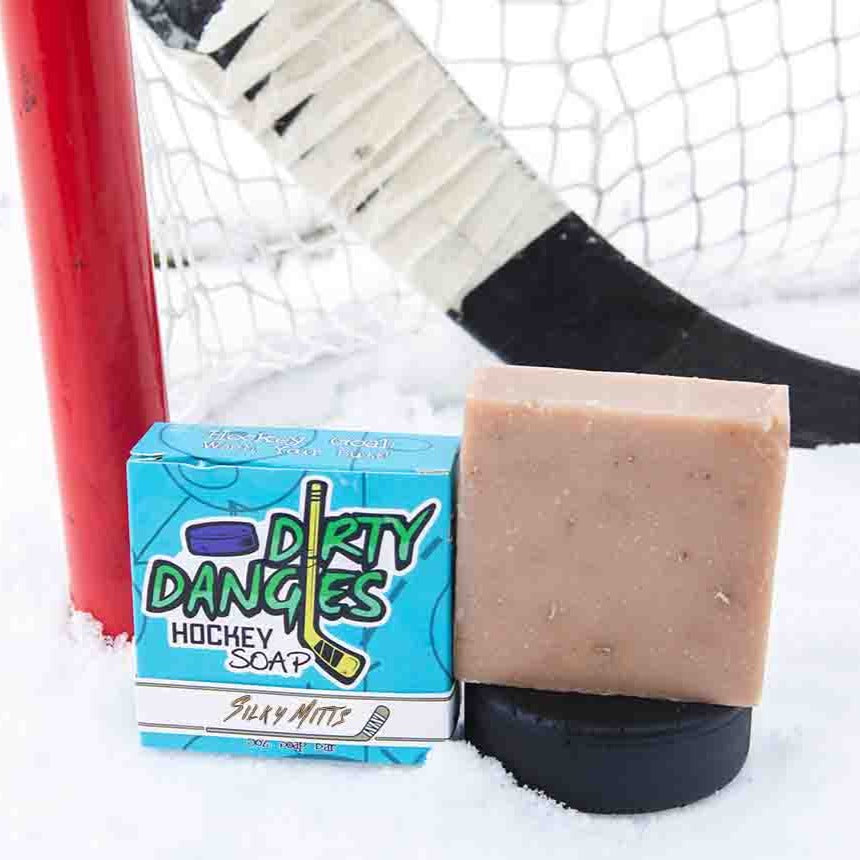 A brown soap bar sits in the snow with a hockey goal, hockey puck and a hockey stick. Silky MItts