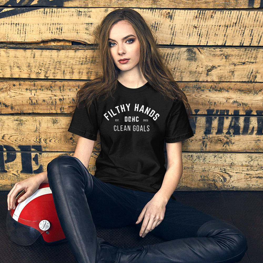 A woman sitting against a wood background wearing a black t shirt. Filthy Hands clean goals ddhc