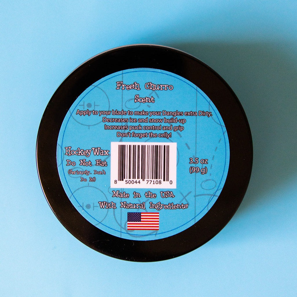 The back of a tin of Dirty Dangles Hockey Stick Wax Fresh Churro Scent sits on a blue background.
