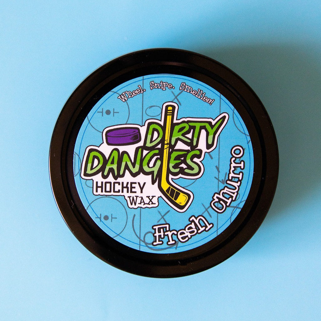 A tin of Dirty Dangles Hockey Stick Wax Fresh Churro Scent sits on a blue background.