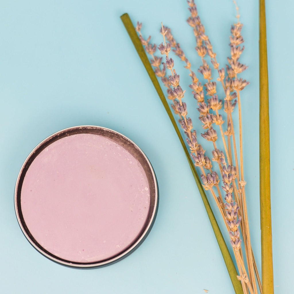 A tin of dirty dangles girls and womens hockey stick wax on a blue background with lavender and lemongrass