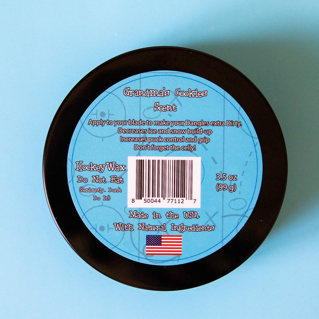 The back of a tin of Dirty Dangles Hockey Stick Wax Grandma's Cookies Scent sits on a blue background.