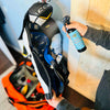 A woman spraying a hockey shin guard with a bottle of Stank Fighter hockey gear deodorizing spray