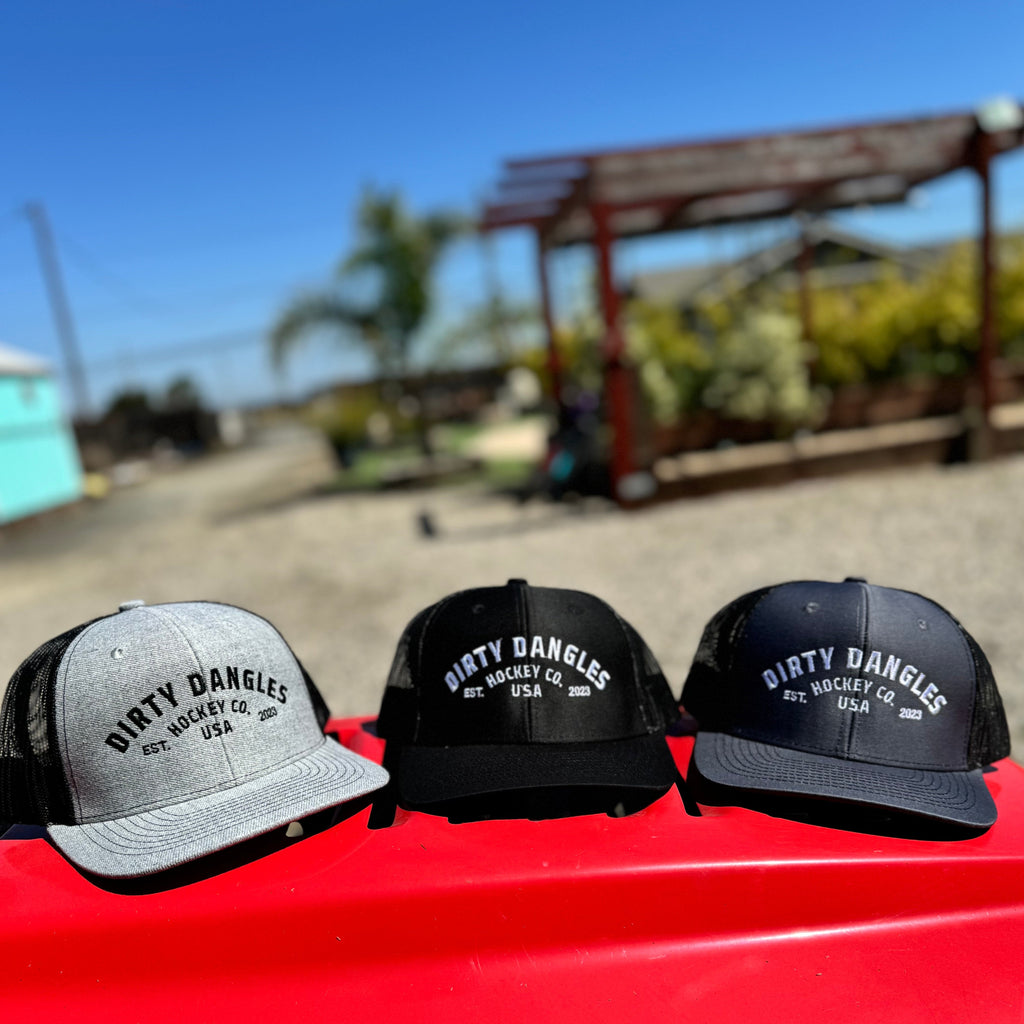 3 dirty dangles hockey co. mesh snapback trucker hats on a red lawn mower. light gray and black, black on black and dark gray on black.