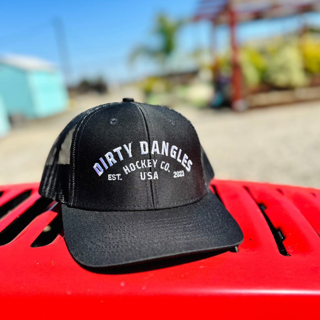 a black dirty dangles hockey co mesh snapback trucker hat outside on a red lawn mower.