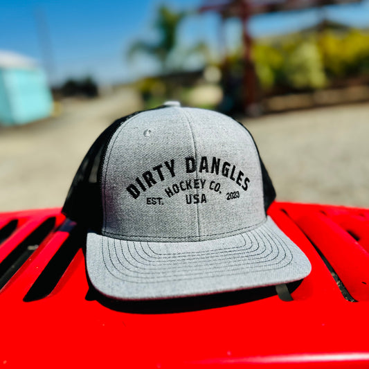 a light gray and black dirty dangles hockey co mesh snapback trucker hat outside on a red lawn mower.