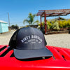 a dark gray and black dirty dangles hockey co mesh snapback trucker hat outside on a red lawn mower.