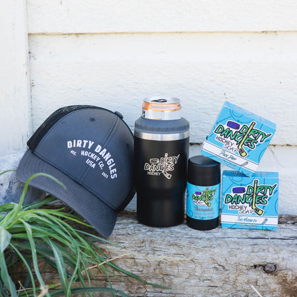 2 bars of hockey soap, a black 2 in 1 drink tumbler can holder, a stick of dirty dangles natural deodorant and a dirty dangles hockey co. hat outside on a piece of wood.