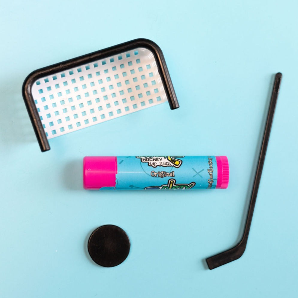 A pink stick of original flavor lip balm on a blue background with small hockey toys. Dirty dangles natural lip balm