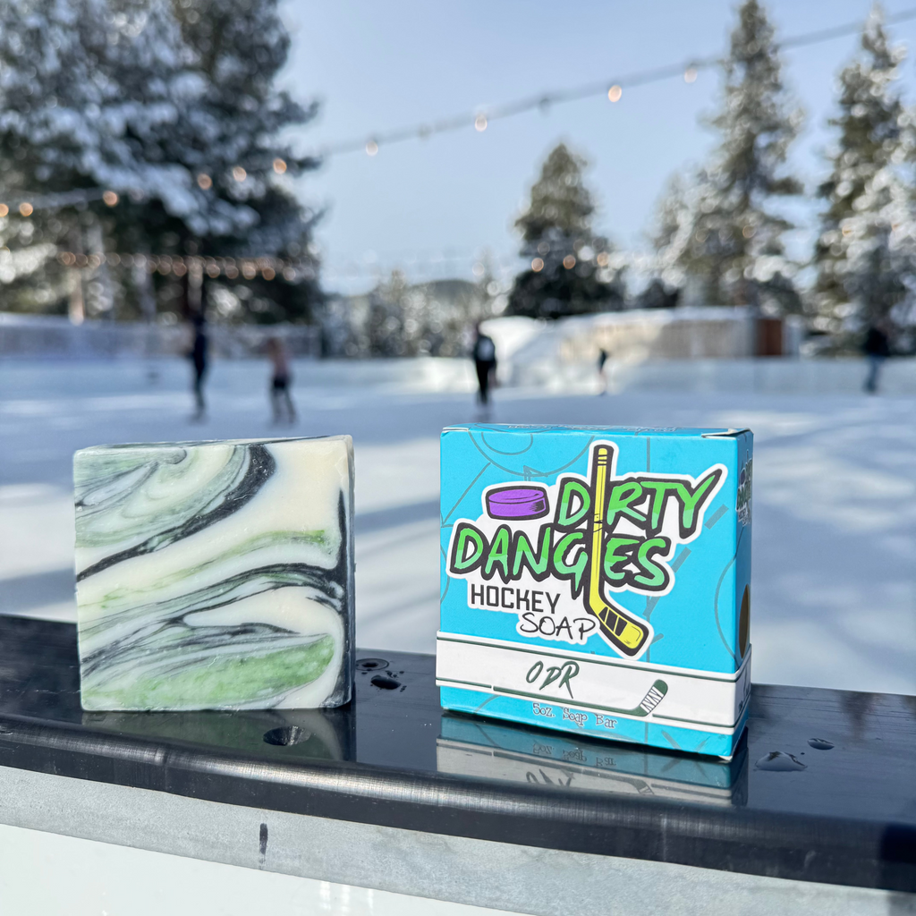A Dirty Dangles hockey soap bar ODR scent on the boards of an outdoor ice rink. A green, black and white swirl soap bar,