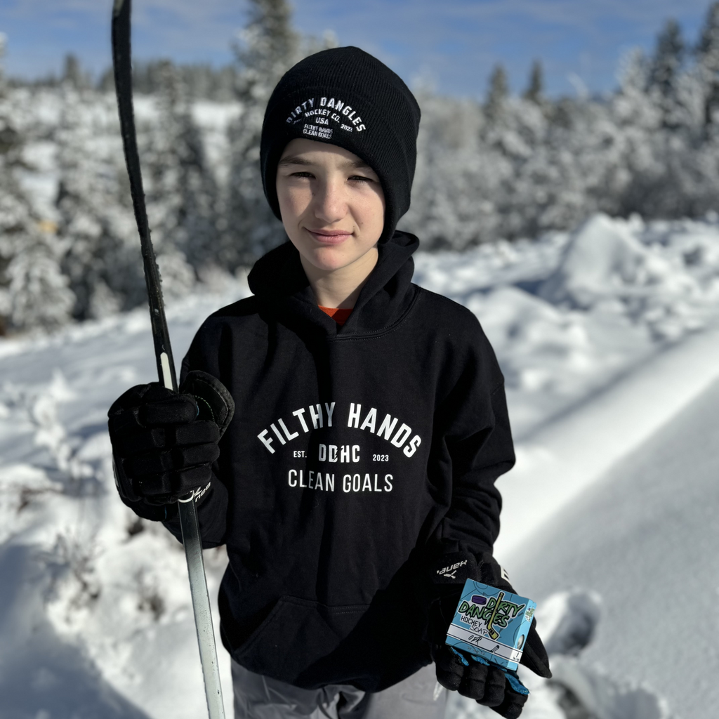 A youth hockey player holding a bar and box of Dirty Dangles ODR soap near an outdoor ice rink.