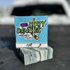 A bar and box of Dirty Dangles ODR soap on the bed of a truck. A green, black and white swirl soap bar,