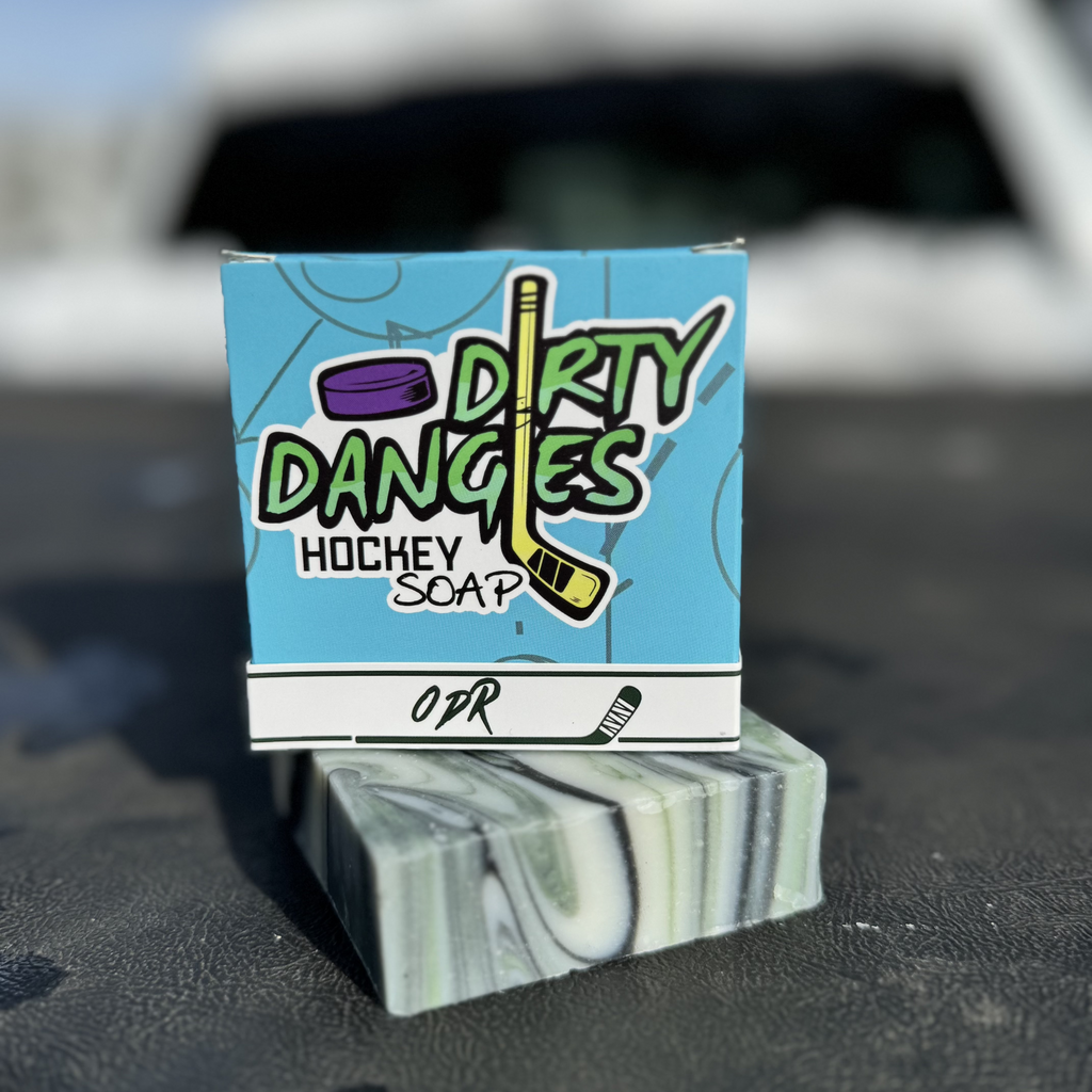 A bar and box of Dirty Dangles ODR soap on the bed of a truck. A green, black and white swirl soap bar,