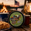 A tin of dirty dangles screamin eagle 4th of july stick wax on a picnic table with apple pie and american flags