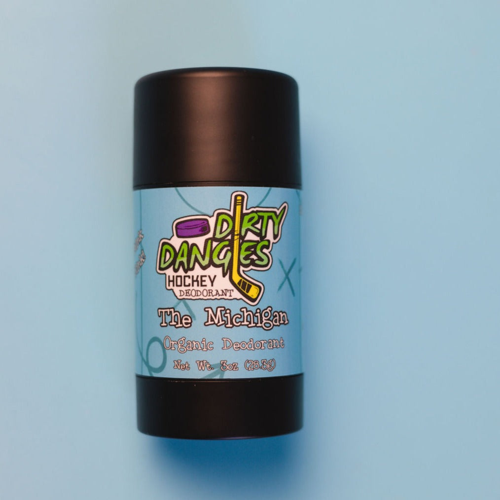 A tube of dirty dangles natural probiotic deodorant on a blue background. The Michigan scent