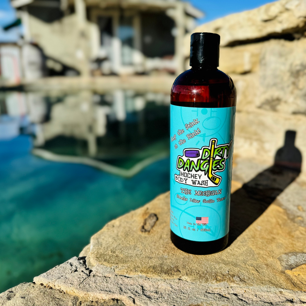 Bottle of Dirty Dangles Hockey Body wash on a rocky surface with water and a dock in the background