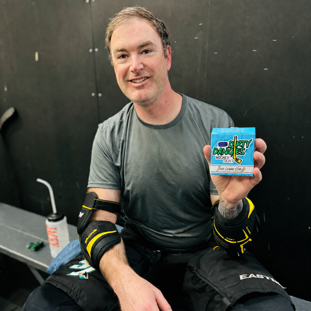 An adult beer league hockey player holding a box of league hero grapefruit pale ale soap while sitting on a bench in hockey gear