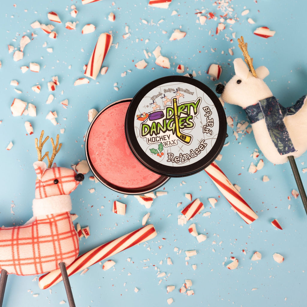 A tin of dirty dangles reindeer farts holiday hockey stick wax on a blue background with candy canes and reindeer