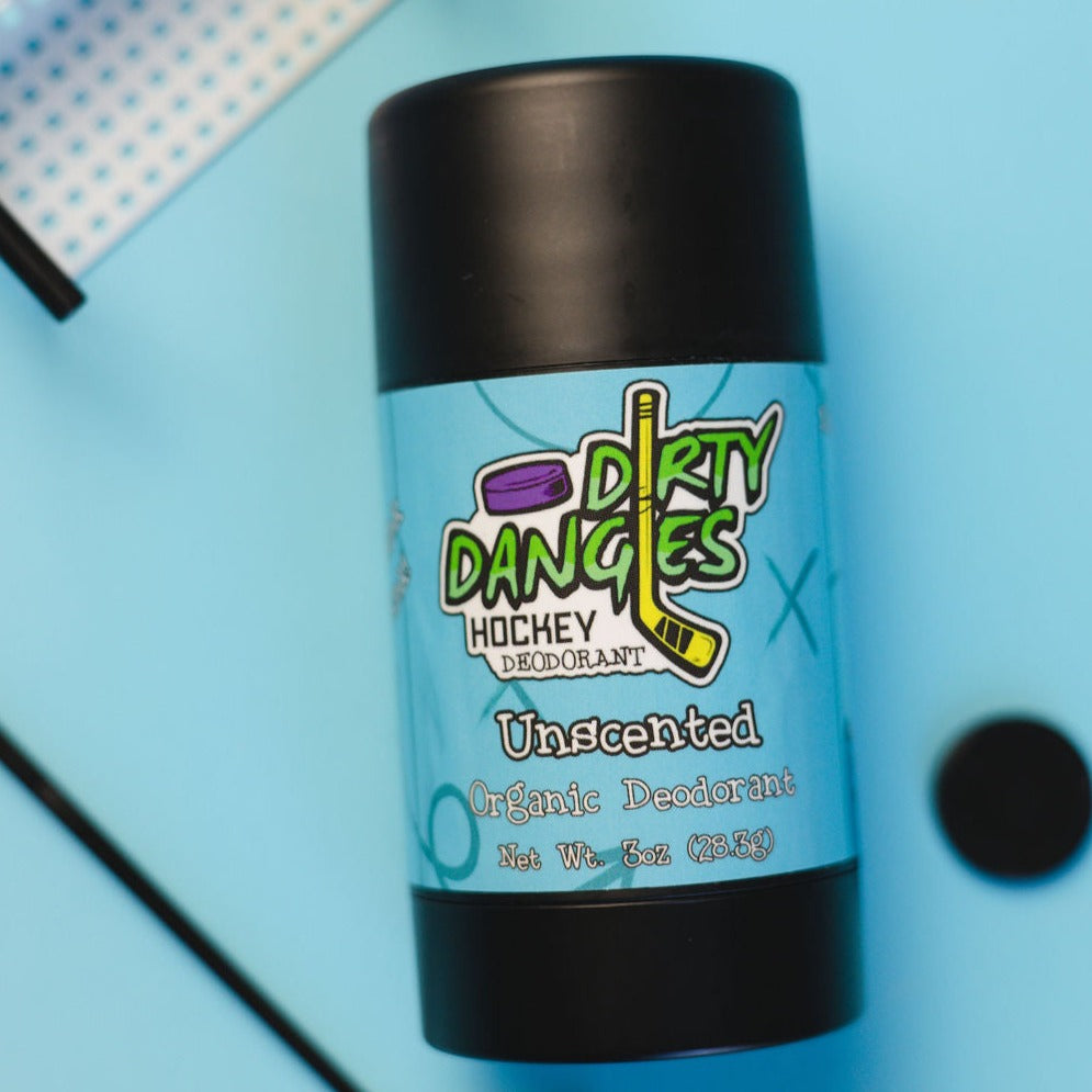 A tube of dirty dangles fragrance free aluminum-free unscented natural hockey deodorant on a blue background with hockey toys